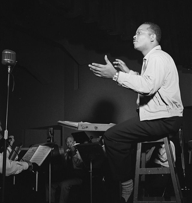 Bandleader Sy Oliver conducting from a chair.